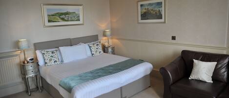 A neatly arranged bedroom with a large bed, two bedside tables, a brown leather armchair, and two framed pictures on the wall.