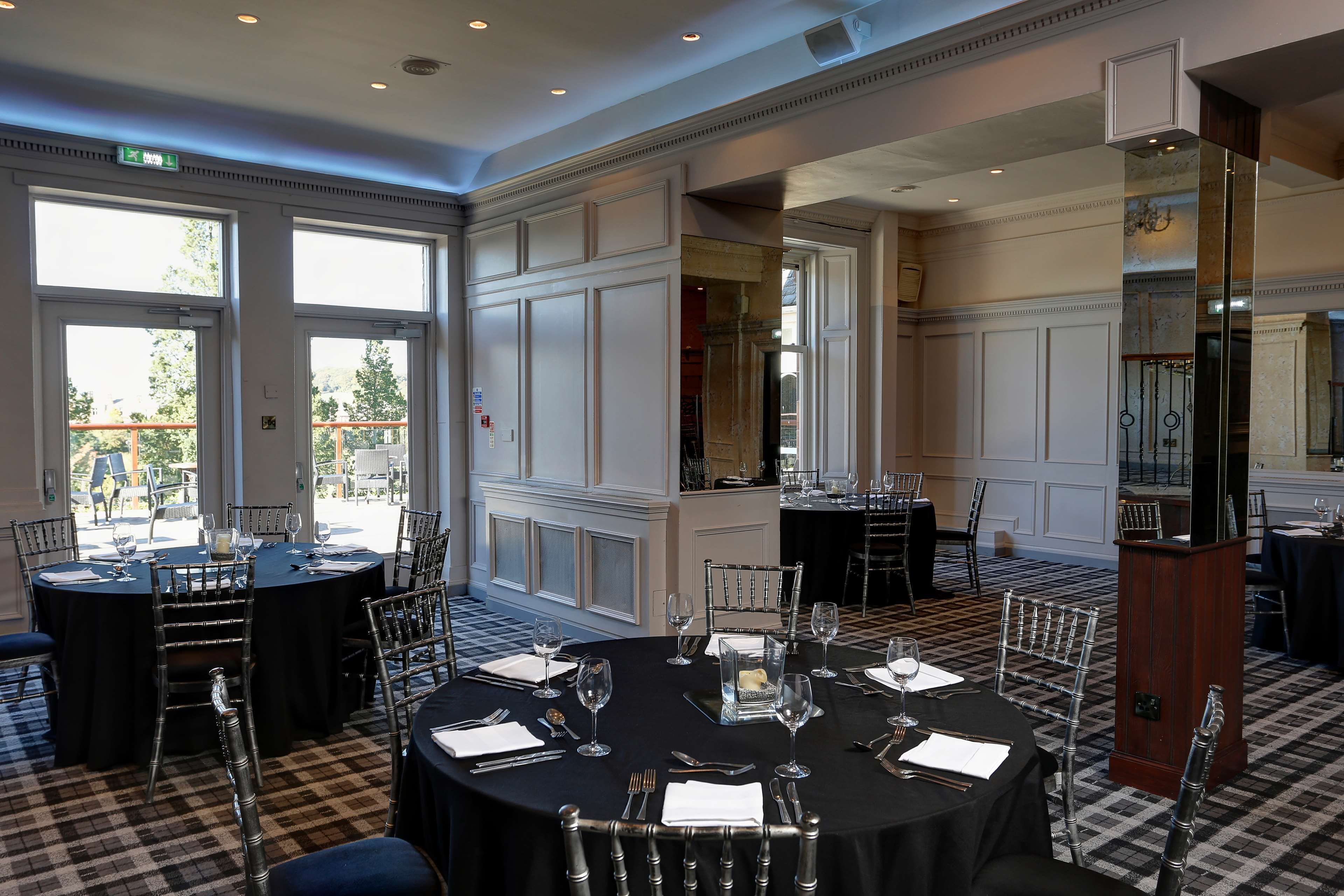 A formal dining room with round tables, black tablecloths, and metal chairs.