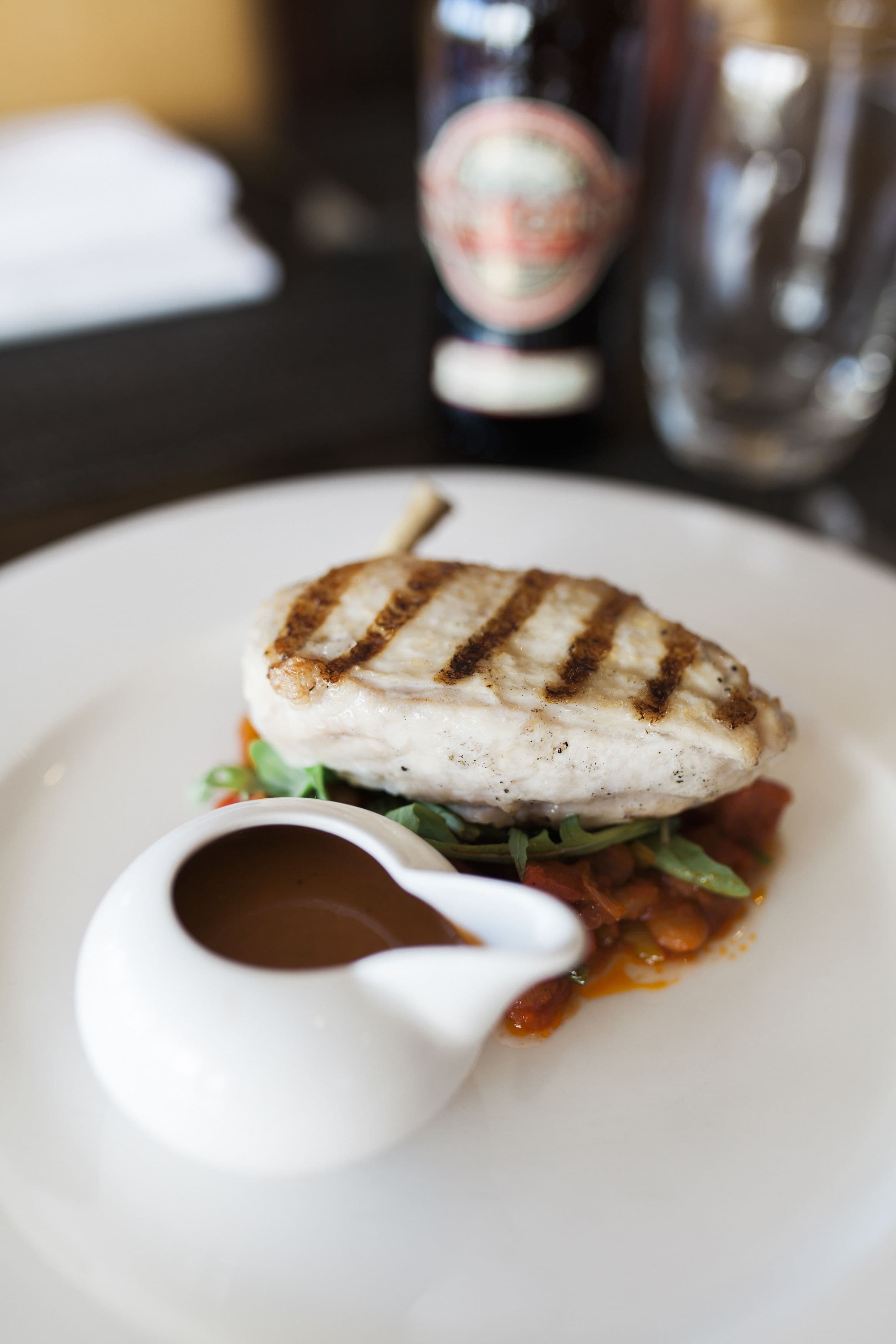 A plate with grilled fish, a small bowl of sauce, and some greens.