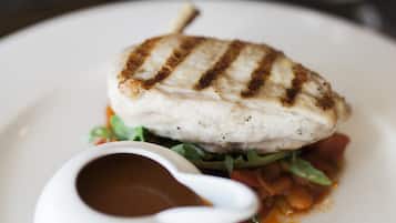 A plate with grilled fish, a small bowl of sauce, and some greens.