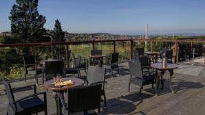 Un patio exterior con mobiliario de mimbre y mesas, con vistas a un campo de golf y una zona residencial.