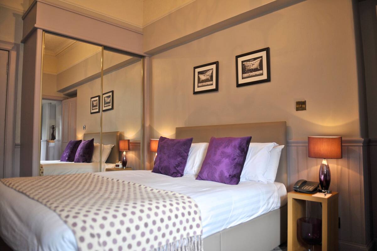 A hotel room with a large bed, a nightstand with a lamp, and two framed pictures on the wall.