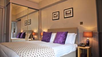 A hotel room with a large bed, a nightstand with a lamp, and two framed pictures on the wall.