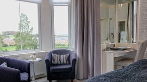 Un dormitorio con vistas a un paisaje verde, un escritorio con un espejo y dos sillones.