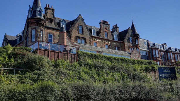 Un edificio histórico con varias torres y un letrero llamativo del Hotel Braid Hills.