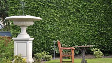A garden with a white fountain, a wooden bench, and a table.
