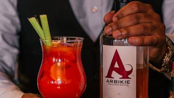 Un cantinero sosteniendo una copa de cóctel con una bebida roja y palitos de apio, y una botella de vodka Arbikie Chilli.