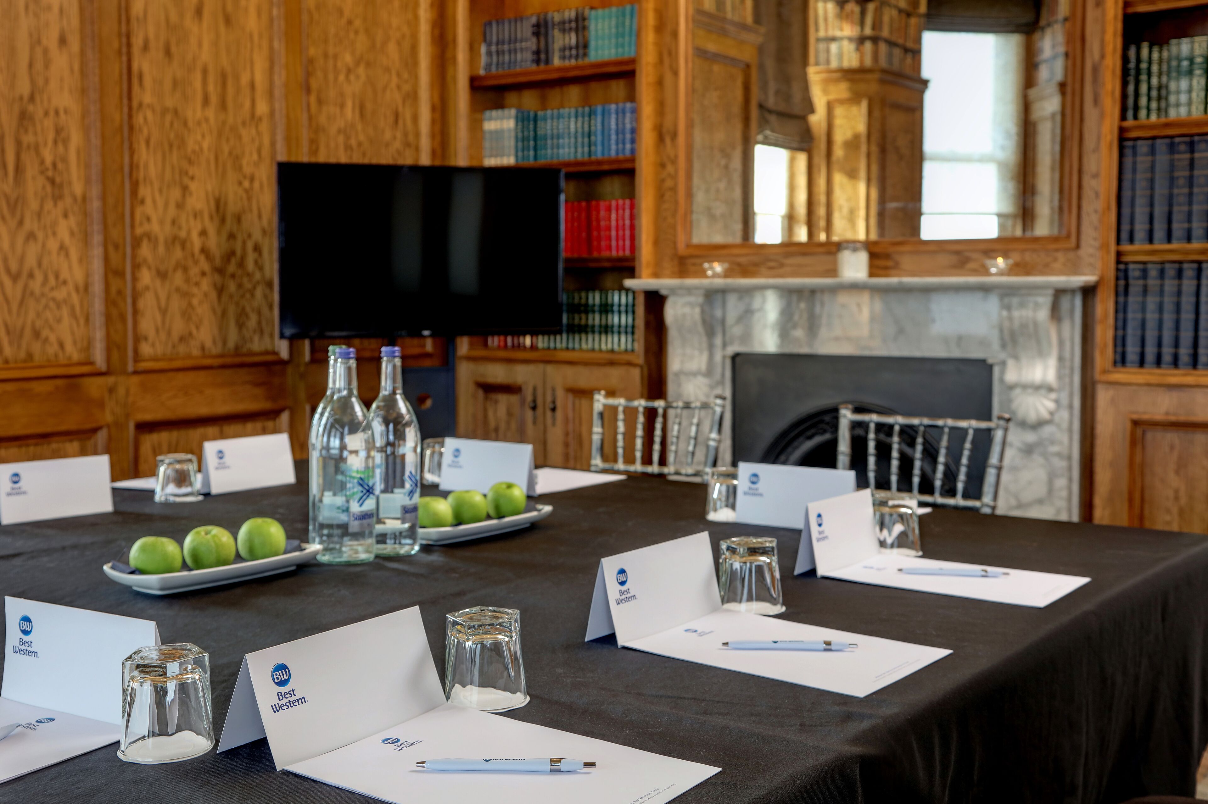 A conference room with a long table set for a meeting, name cards, a television, and a fireplace.