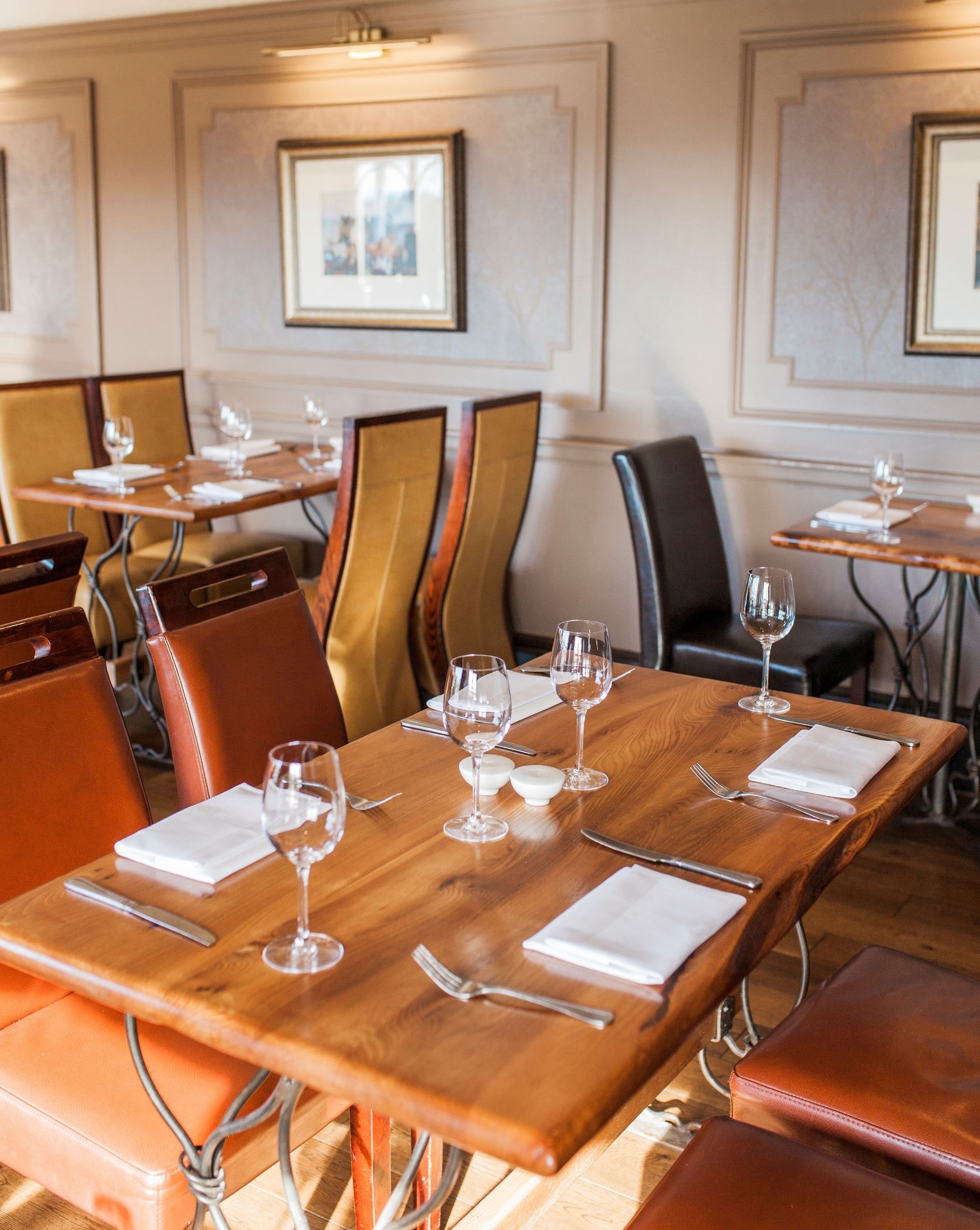 Een restaurant met houten tafels en stoelen, elk gedekt met wijnglazen, bestek en servetten.