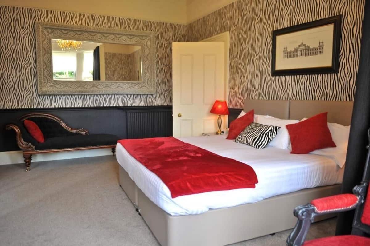 A bedroom with a bed, a chair, a sofa, a mirror, and a door.