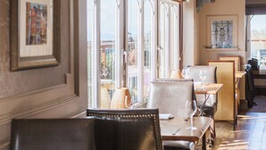 Interior de restaurante con mesas y sillas de madera, ventanas amplias y vistas al exterior.