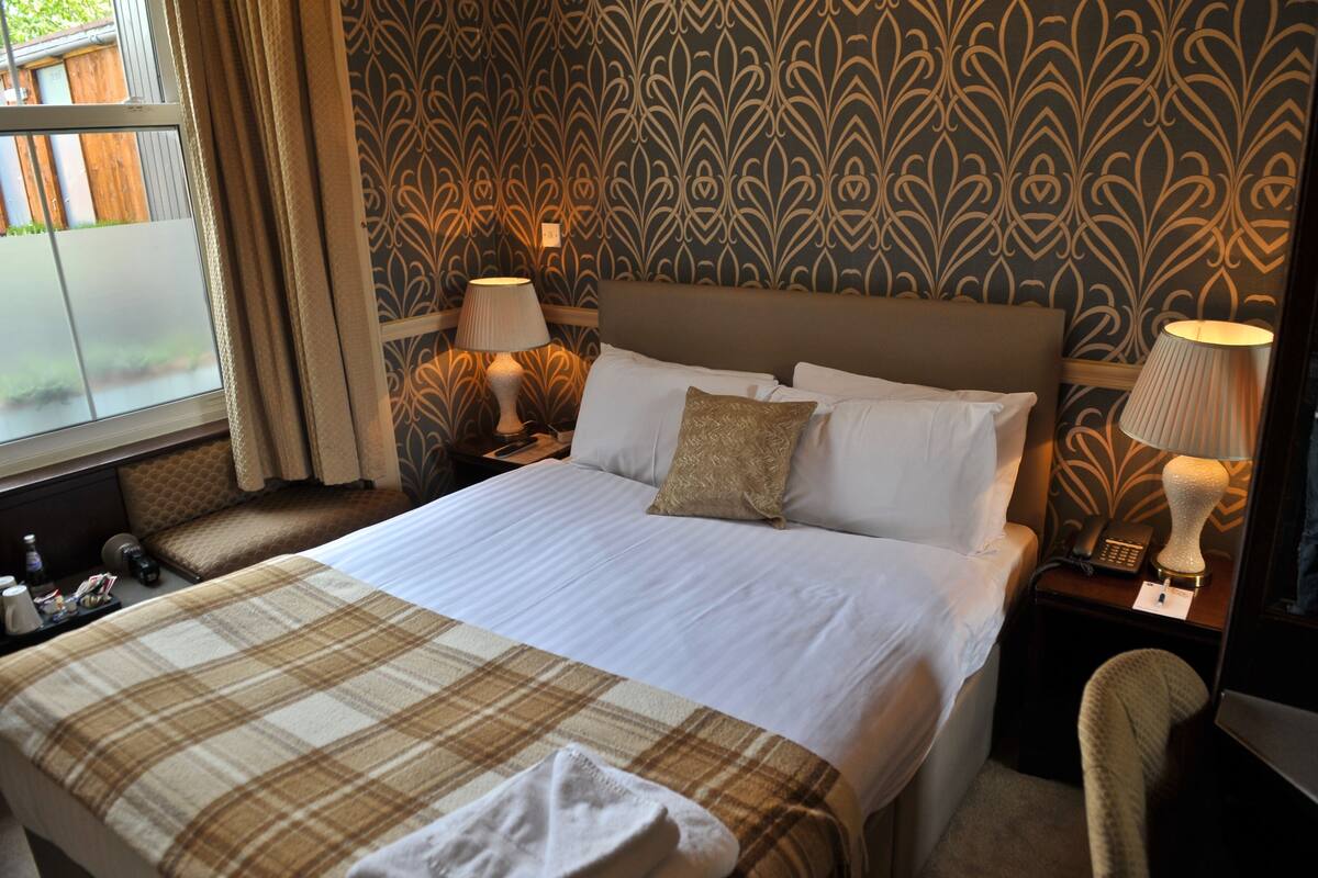 A hotel room with a large bed, two bedside tables with lamps, a chair, and a window with curtains.