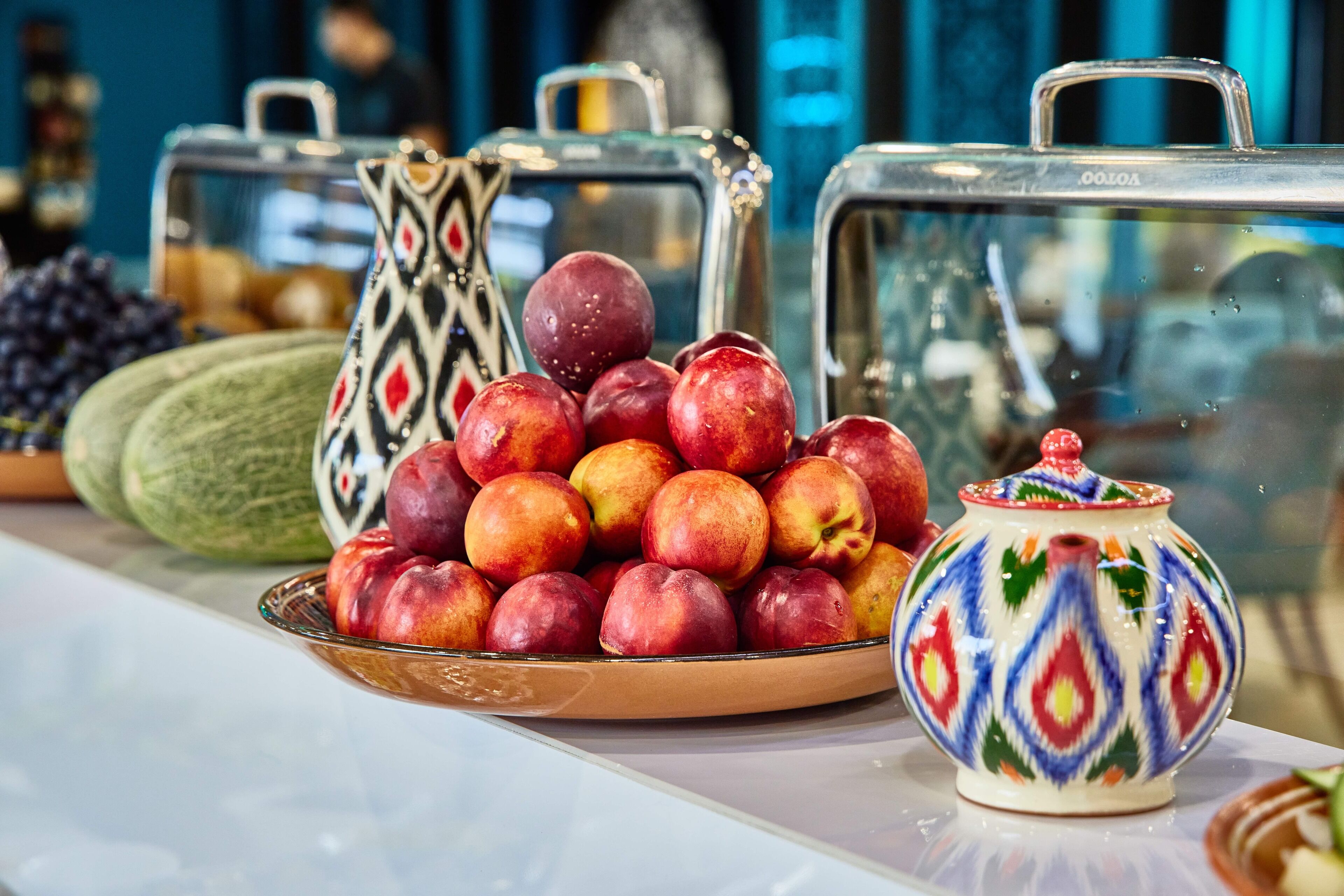 A buffet table with a variety of fruits and a decorative ceramic jug.