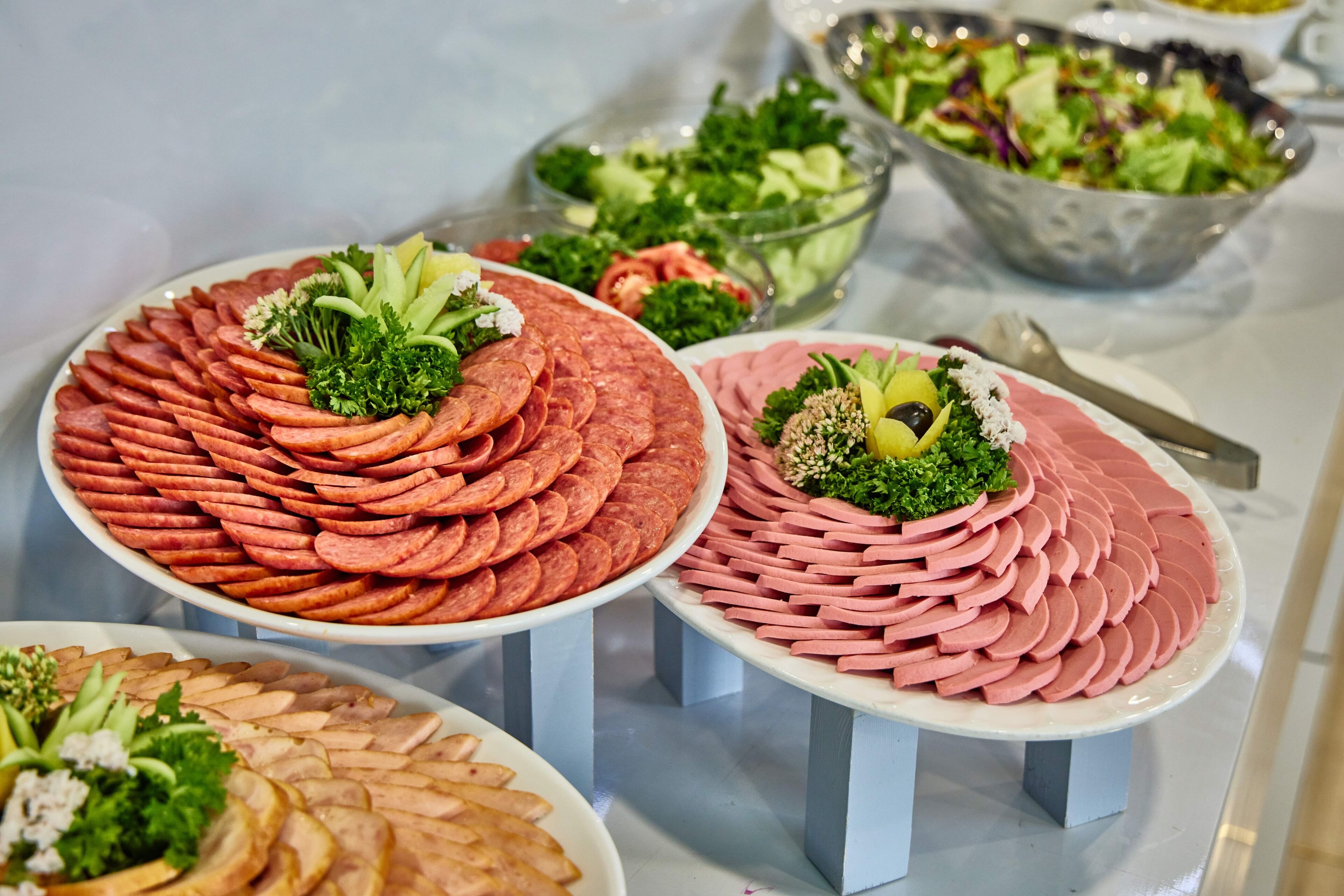 A buffet table with neatly arranged meat platters, salad bowls, and a variety of vegetables.