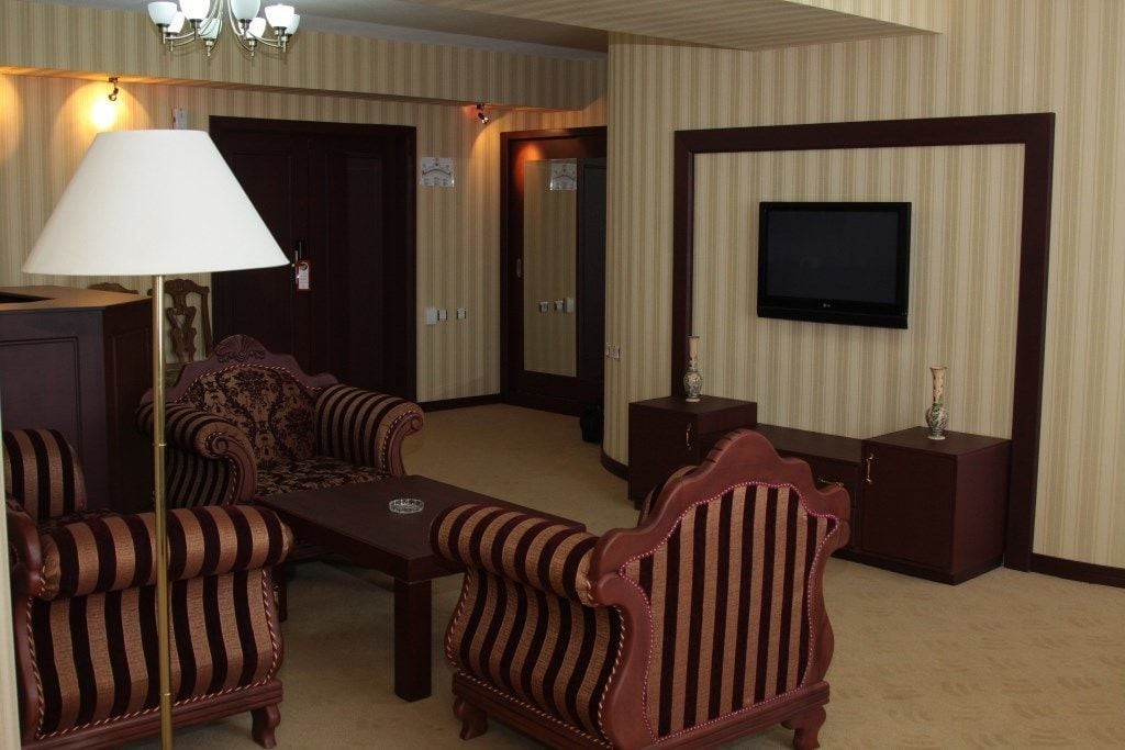 Une chambre d’hôtel avec des meubles rembourrés à rayures, un téléviseur à écran plat fixé au mur et une lampe sur une table d’appoint.