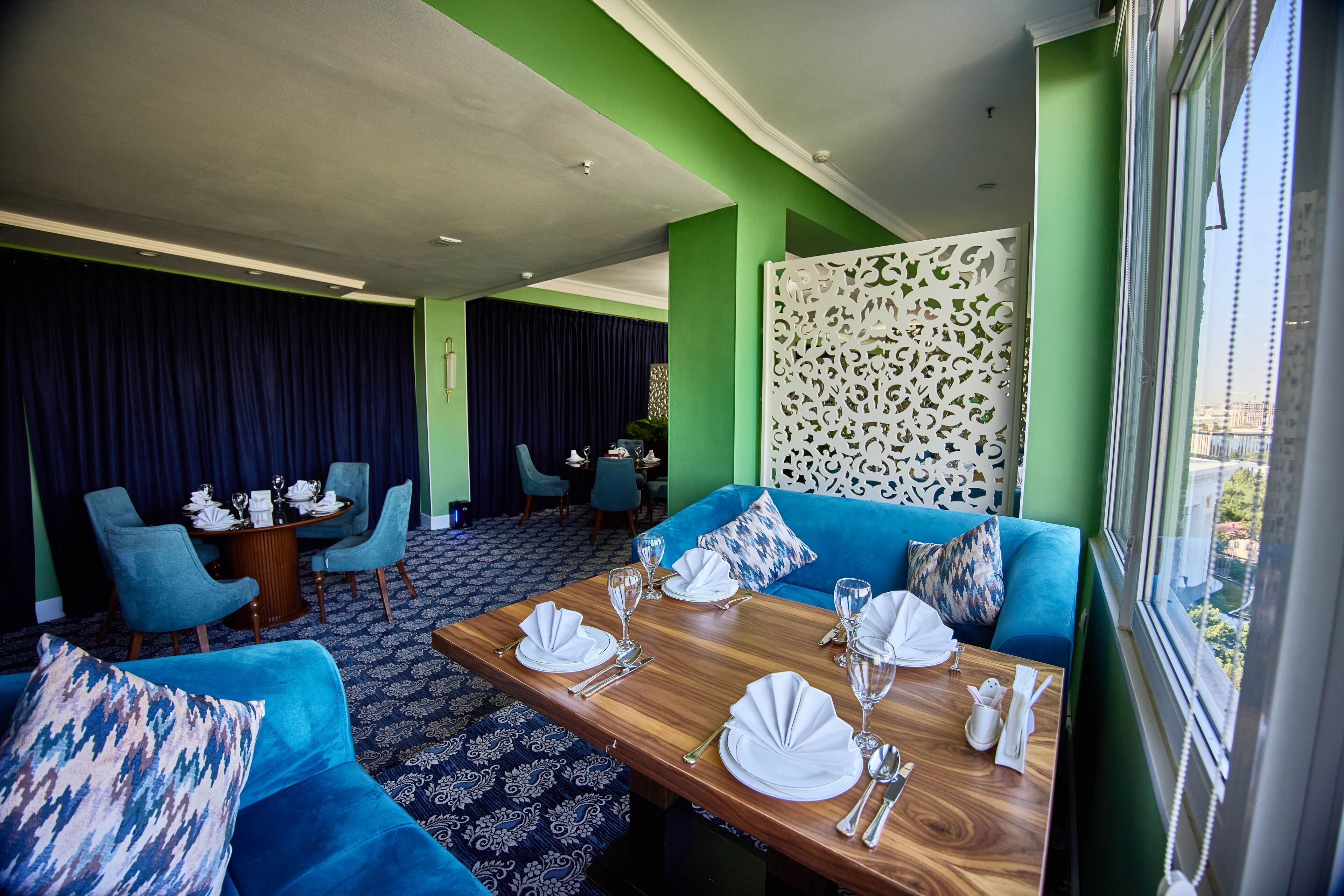 Un comedor con una mesa de madera dispuesta para cuatro personas, asientos tapizados en azul y un panel decorativo blanco.