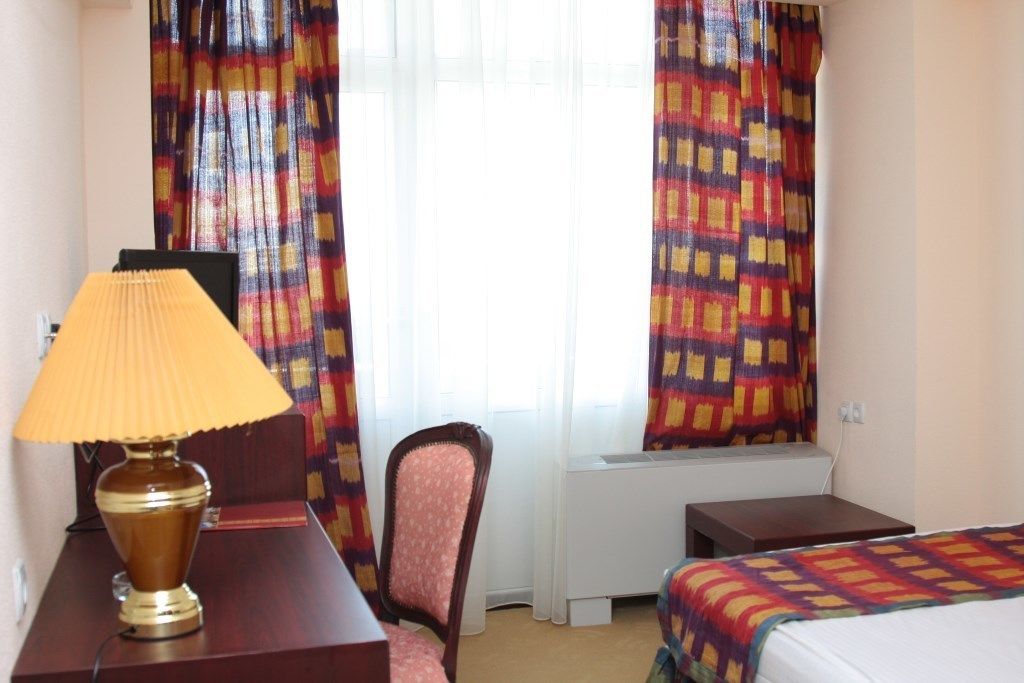 A hotel room with a bed, a desk with a lamp, a chair, and a radiator.