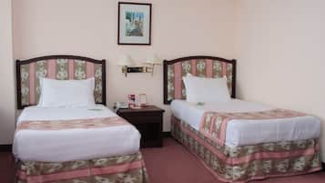 A hotel room with two beds, each with a patterned bedspread and matching headboards. There is a nightstand with lamps and a framed picture on the wall above the beds.