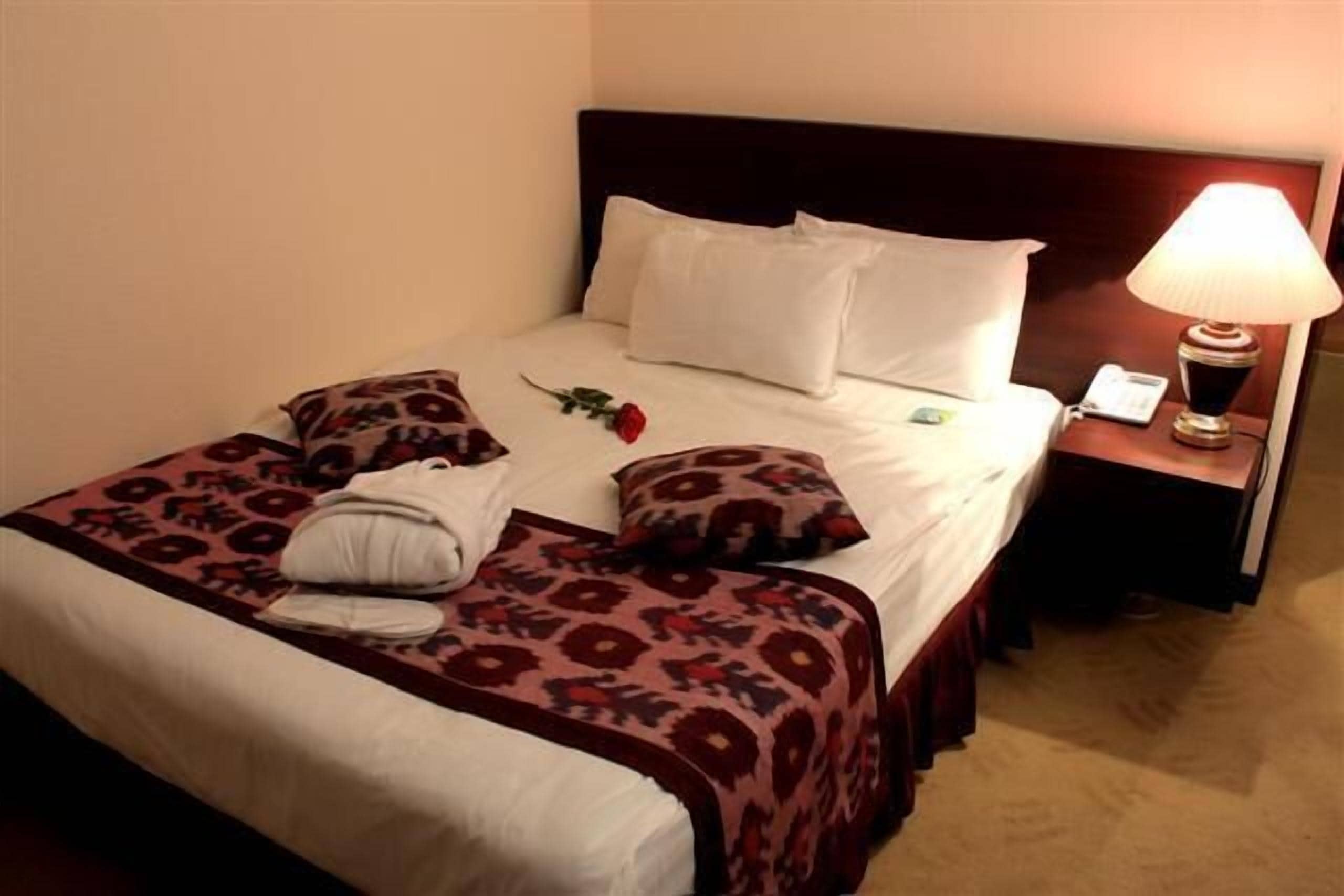 A neatly made bed with a floral bedspread, white pillows, and a single red rose.