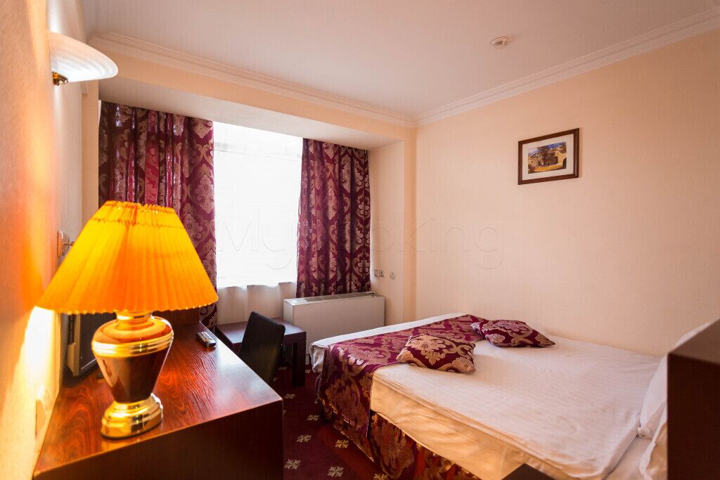 Habitación de hotel con cama, escritorio con lámpara, una silla y ventana con cortinas.