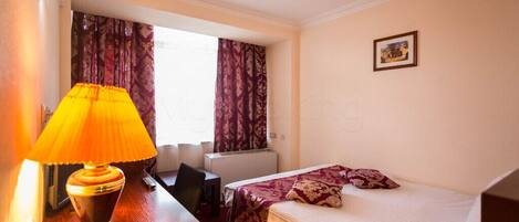 Habitación de hotel con cama, escritorio con lámpara, una silla y ventana con cortinas.