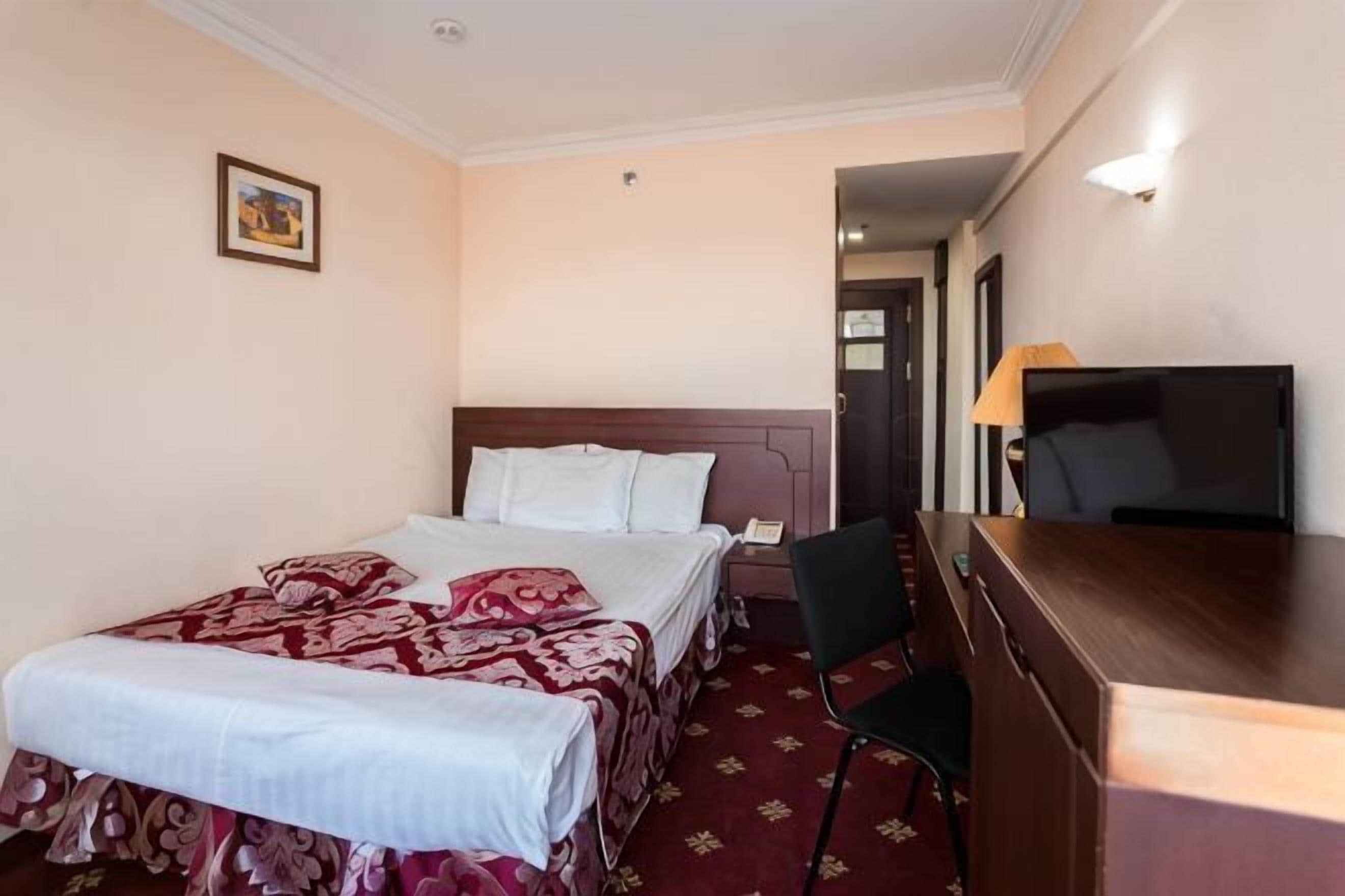 A hotel room with a bed, a desk, a chair, a television, and a door.