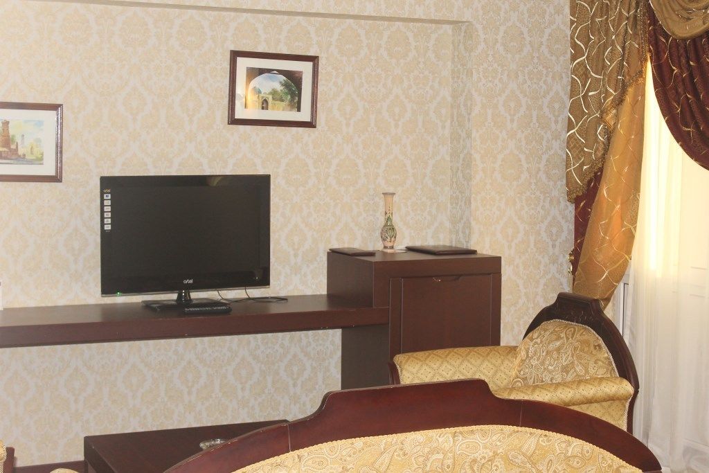 A hotel room with a television on a stand, a small table with a vase, and a bed with a patterned bedspread.