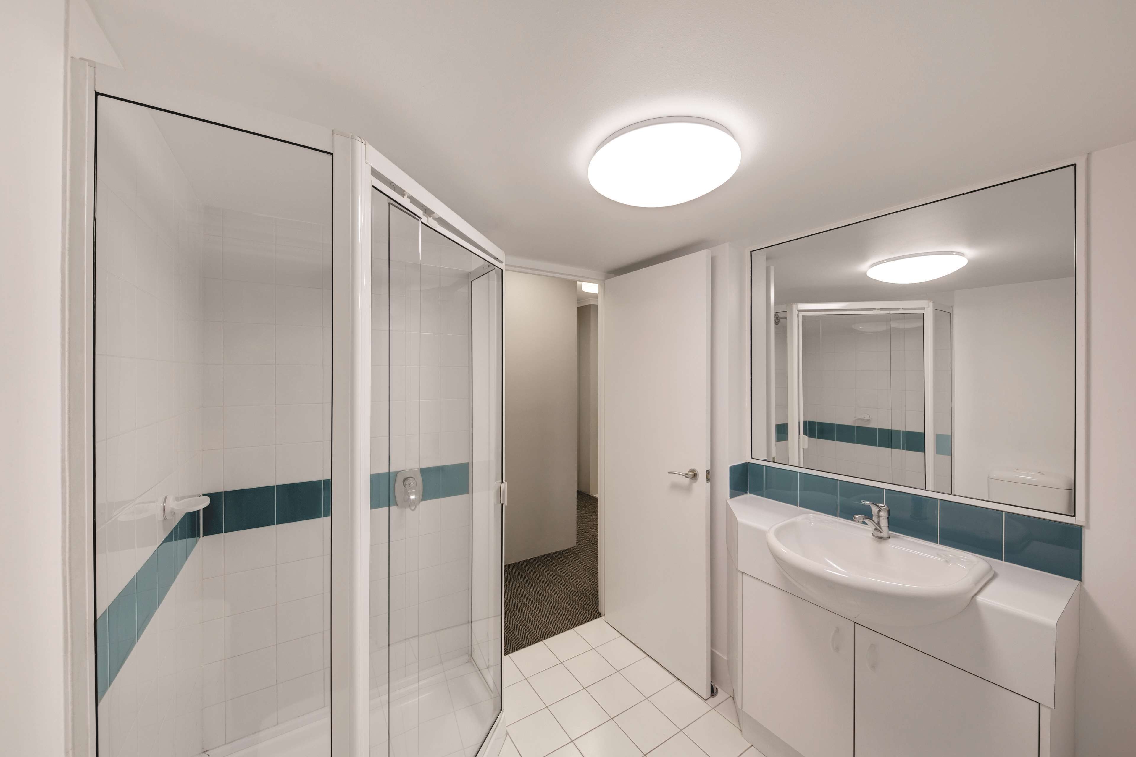 A modern bathroom with a glass shower enclosure, a white sink with a blue tile backsplash, and a large mirror.