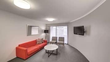 A modern living room with a red sofa, two armchairs, a coffee table, a flat-screen TV, and large windows with sheer curtains.