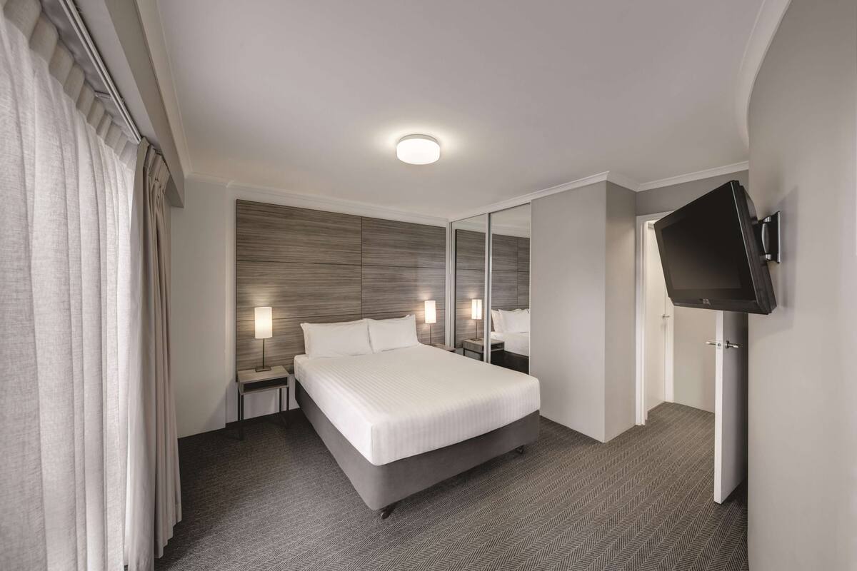 A hotel room with a large bed, bedside lamps, a flat-screen TV mounted on the wall, and a mirror.