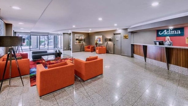 A hotel lobby with orange seating, a reception desk, and a large window offering a view.