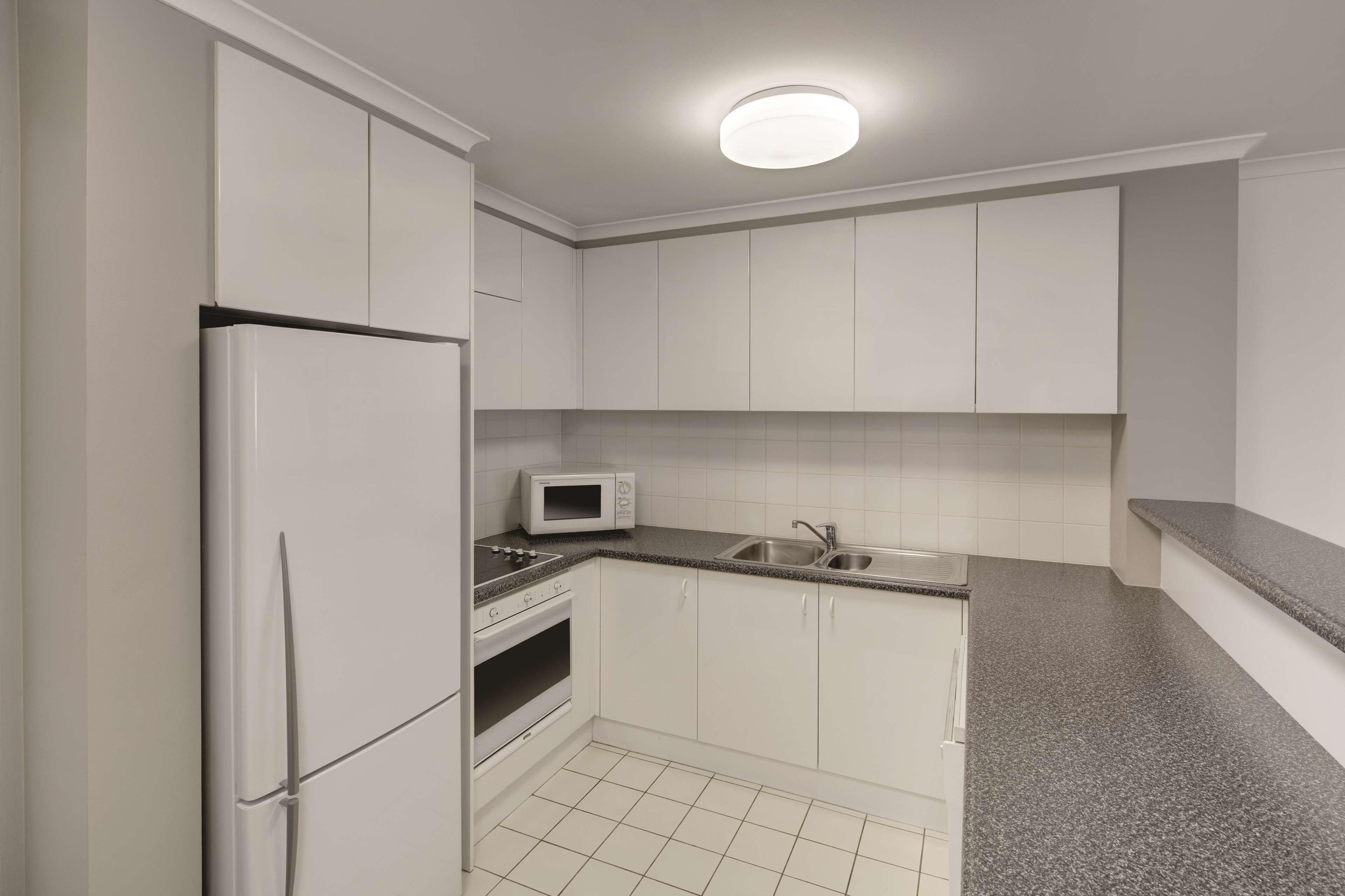 A compact kitchen with white cabinets, a built-in microwave, a stainless steel sink, and a granite countertop.