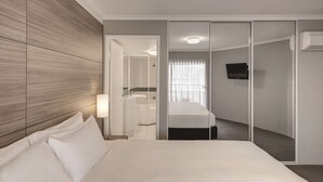A hotel room with a large bed, a separate bathroom, a TV, and a sliding door closet.