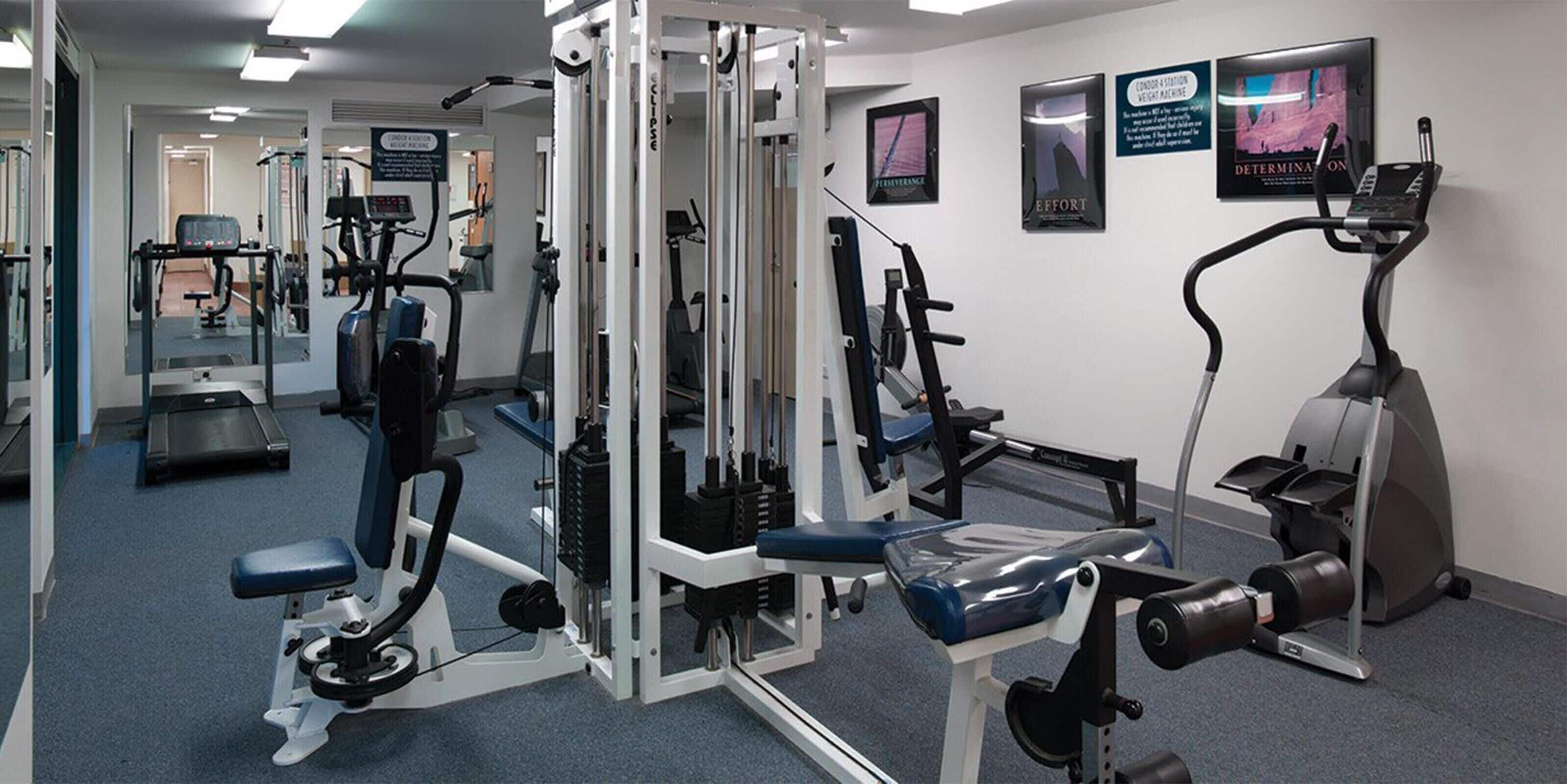 A gym with cardio machines, weight training equipment, and motivational posters on the walls.