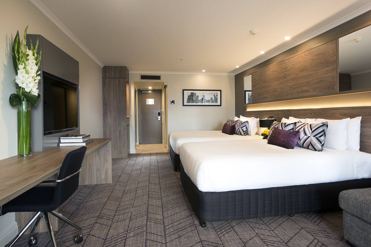 A hotel room with a large bed, a desk, a chair, a mirror, and a vase with flowers.