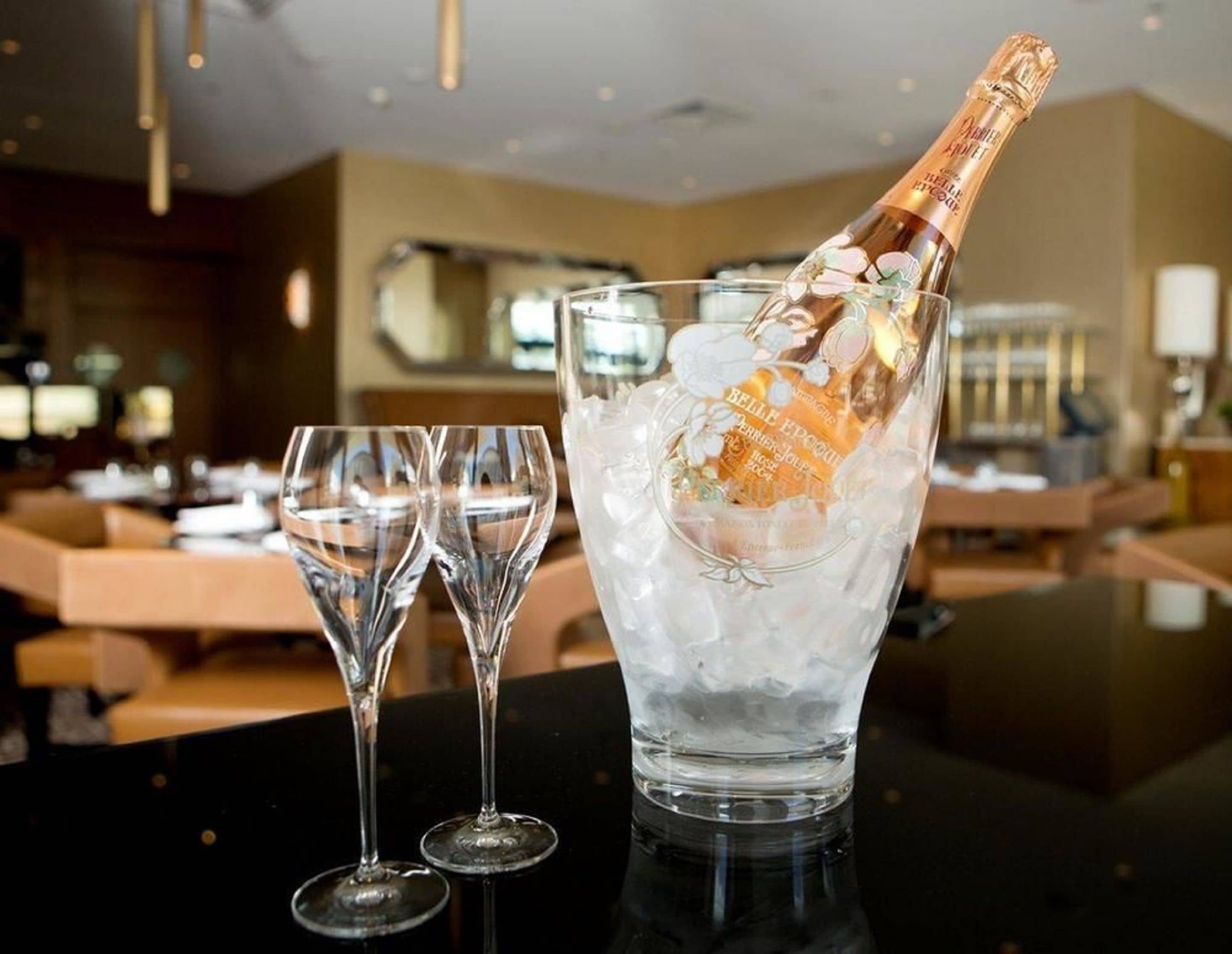 A bottle of champagne in a glass with ice cubes, placed on a table in a restaurant setting.