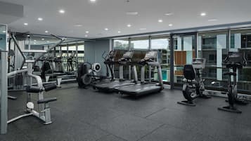 A modern gym with various exercise equipment, large windows, and a spacious layout.