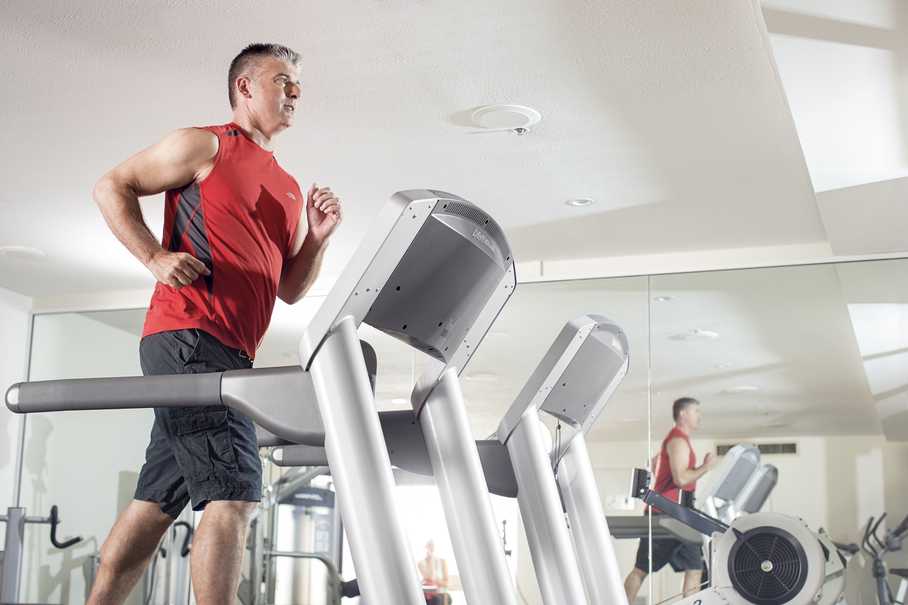 A man running on a treadmill in a gym with a mirror reflecting his image.