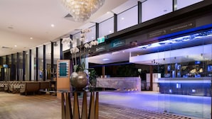 A modern hotel lobby with a reception desk, seating area, and a view of the restaurant. - Rydges South Bank (South Brisbane)