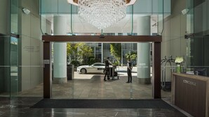 A modern hotel lobby with a glass entrance, a reception desk labeled "CONCIERGE", and a white car parked outside. - Rydges South Bank (South Brisbane)