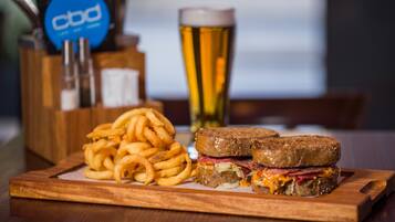 Un sándwich, una cerveza en un vaso y un recipiente con aros de cebolla sobre una tabla de madera.