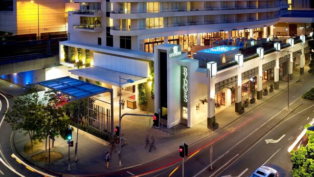 A multi-story hotel with a curved facade, outdoor seating areas, and a visible entrance. - Rydges South Bank (South Brisbane)