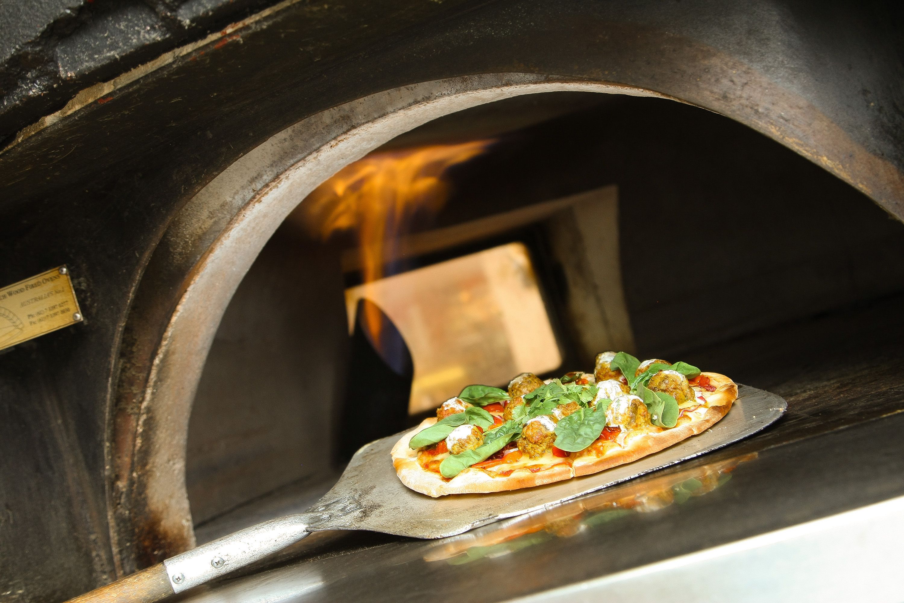 Pizza dentro de um forno a lenha, em uma bandeja de metal.