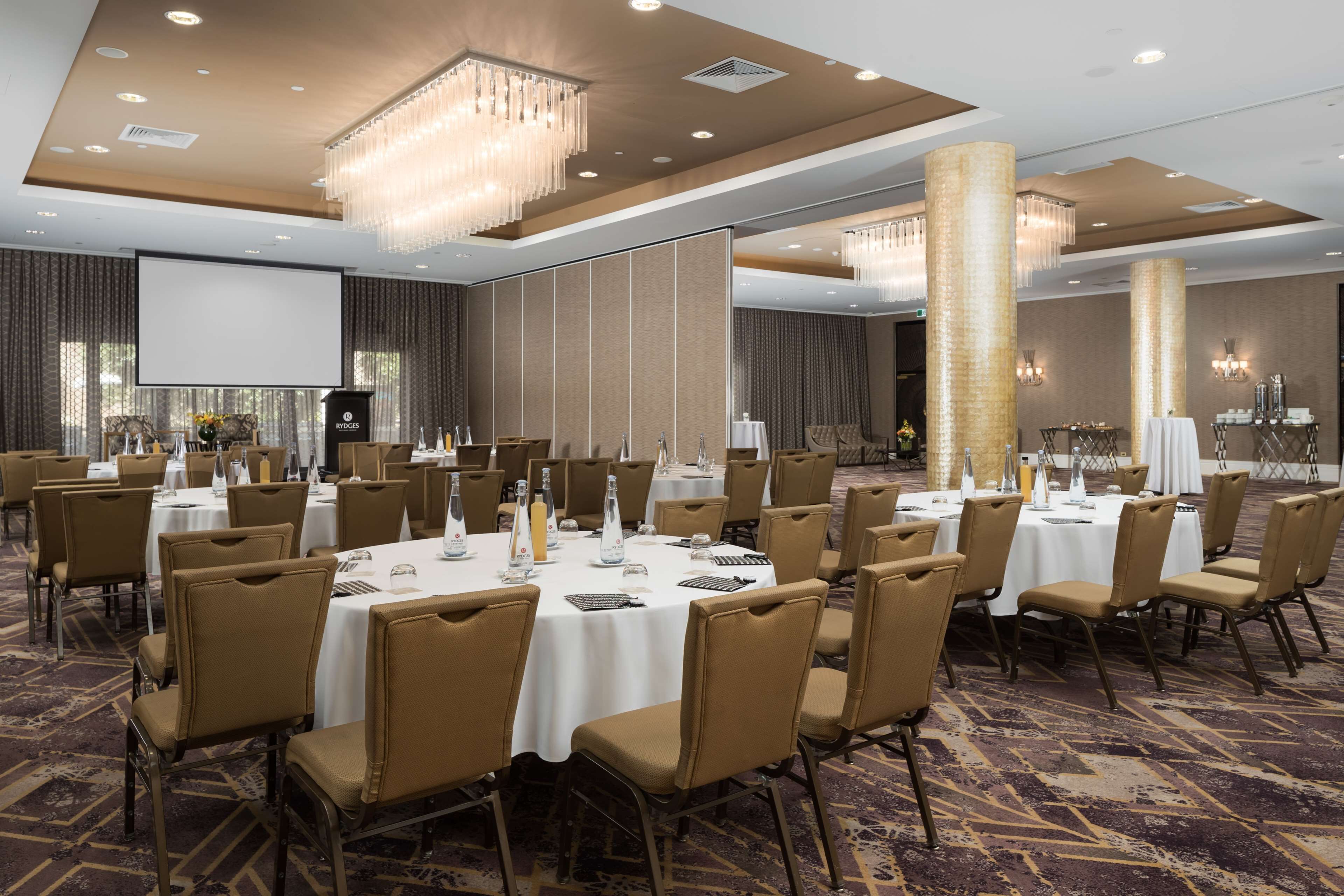 Une salle de conférence avec des tables rondes, des chaises de couleur beige et un grand écran.