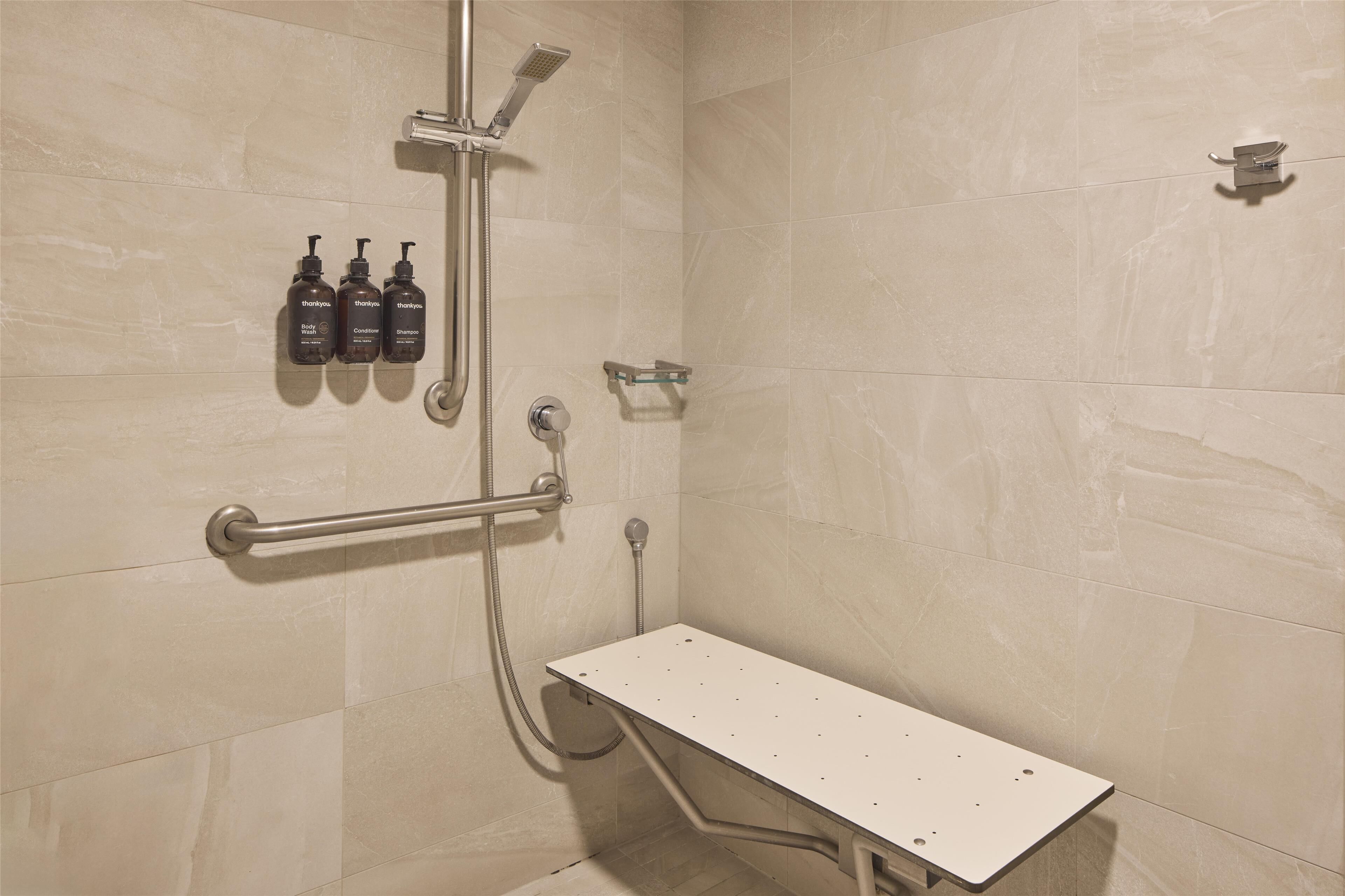 Un baño moderno con ducha, barra de apoyo y tres botellas de champú y acondicionador en la pared.