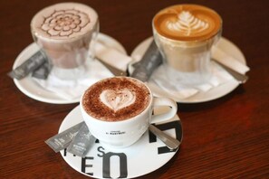 Three cups of coffee with latte art on white saucers, each with a spoon and a packet of creamer. - Rydges South Bank (South Brisbane)