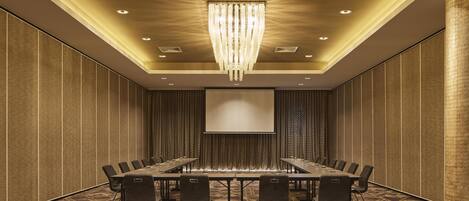 A conference room with a large table, chairs, a projector screen, and a chandelier.