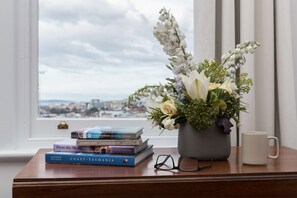 A wooden table with a vase of flowers, a stack of books, a pair of glasses, and a white mug.