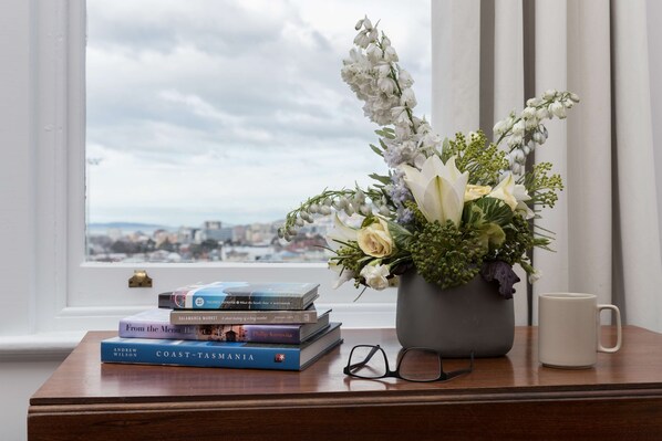 A wooden table with a vase of flowers, a stack of books, a pair of glasses, and a white mug.