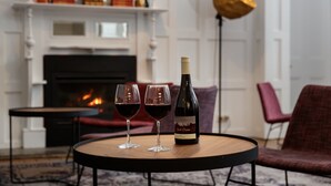 Una habitación con chimenea, dos copas de vino y una botella sobre una mesa redonda.
